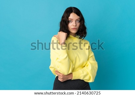 Teenager Ukrainian girl isolated on blue background unhappy and pointing to the side
