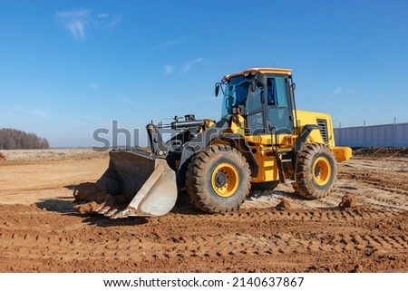 Bulldozer or loader moves the earth at the construction site against the blue sky. An earthmoving machine is leveling the site. Construction heavy equipment for earthworks Royalty-Free Stock Photo #2140637867