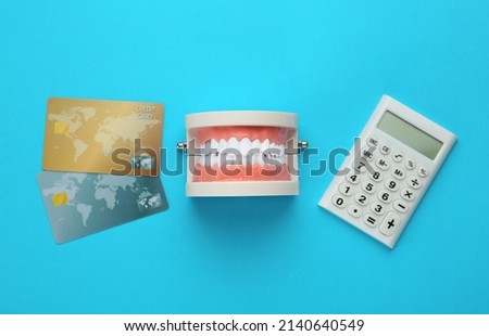 Educational dental typodont model, credit cards and calculator on light blue background, flat lay. Expensive treatment