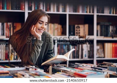Portrait of a pretty smiling girl reading book while buying in a bookstore. Choosing a good book to buy in a bookstore. Woman interested in a book. Royalty-Free Stock Photo #2140650917