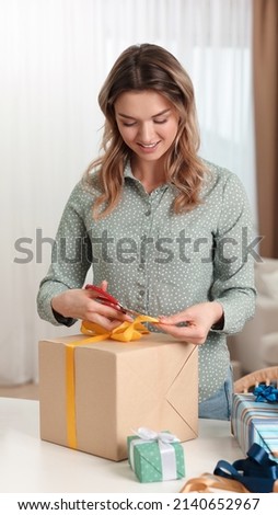 Beautiful young woman wrapping gift at table indoors Royalty-Free Stock Photo #2140652967