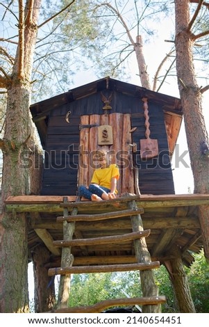 Pretty ten years old girl playing in beautiful creative handmade treehouse in backyard, summer activity, cottagecore, happy summertime in countryside, ecological outdoor playground Royalty-Free Stock Photo #2140654451