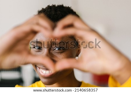 Portrait of young smiling lovely multiracial woman showing shape heart with hands and looking through it with toothy smile while posing at her home - Love and happy people concept Royalty-Free Stock Photo #2140658357