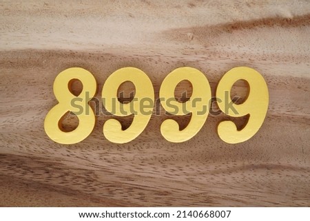 Wooden  numerals 8999 painted in gold on a dark brown and white patterned plank background.