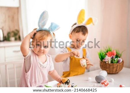 A little girl and a boy of European appearance in rabbit ears draw Easter eggs on their heads. Easter concept. Preparation for Easter. happy Easter