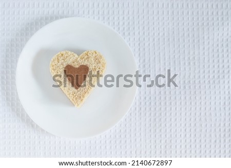 Top view of a heart-shaped cake sprinkled with cocoa lying on a white plate over a white tablecloth background