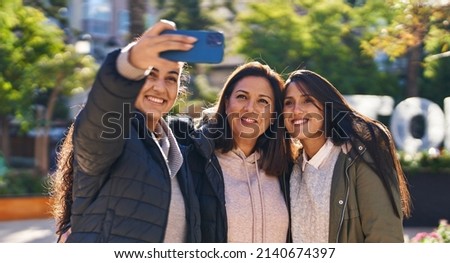 Three woman mother and daughters make selfie by the smartphone at park