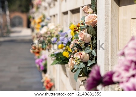 Italian wall cemetery with tombstones and artificial flowers on a sunny summer day in Venice, Italy, Island of San Michele. Commemoration of the dead, deaths of pandemic. Royalty-Free Stock Photo #2140681355