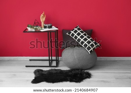 Modern pouf and table near color wall in room