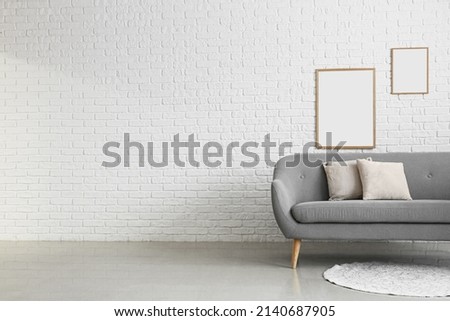 Comfortable sofa and blank photo frames on white brick wall in room interior