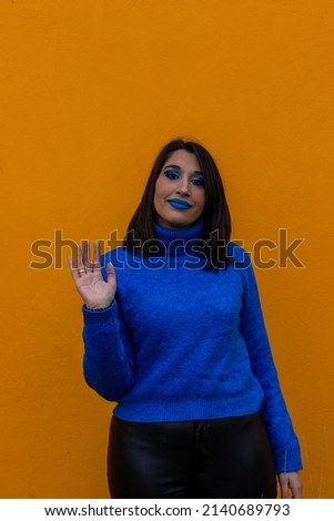 vertical Close up young excited smiling friendly cool caucasian woman 20s with blue make up and blue t-shirt waving hands say hello isolated on yellow color background studio portrait