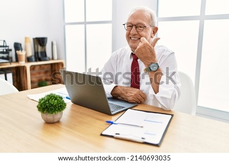 Senior man working at the office using computer laptop doing happy thumbs up gesture with hand. approving expression looking at the camera showing success. 