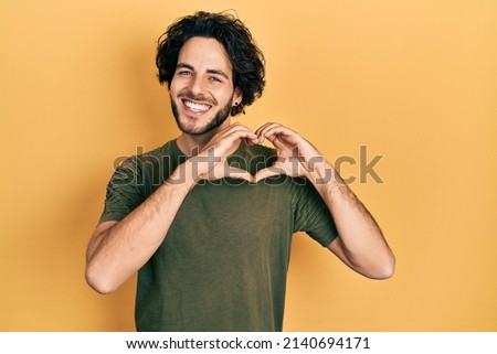 Handsome man wearing casual green t shirt smiling in love doing heart symbol shape with hands. romantic concept. 