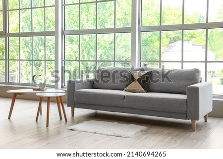 Grey sofa with pillow and tables near big window