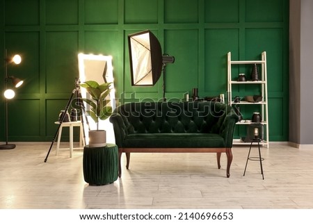 Interior of modern photo studio with sofa, glowing mirror and professional equipment