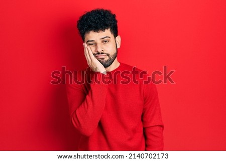 Young arab man with beard wearing casual red sweater thinking looking tired and bored with depression problems with crossed arms. 