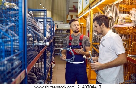 Seller in building materials store advises buyer on hoses for washing machines or dishwashers. Seller and customer are talking standing between shelves in store. Hardware shopping concept. Royalty-Free Stock Photo #2140704417