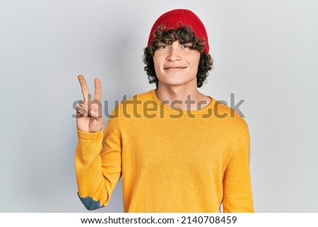Handsome young man wearing wool hat showing and pointing up with fingers number two while smiling confident and happy. 
