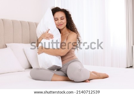 Happy African American woman hugging soft pillow on bed at home Royalty-Free Stock Photo #2140712539
