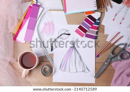 Sketches of clothes and different stuff on wooden table, flat lay. Fashion designer's workplace