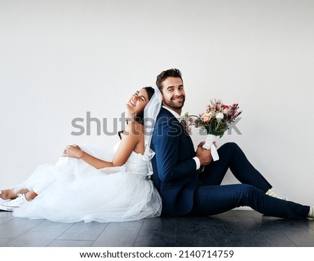 You can lean on me any day. Studio shot of a newly married young couple sitting back to back on the floor against a gray background. Royalty-Free Stock Photo #2140714759