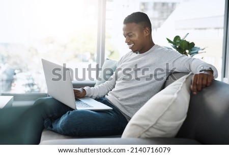Where do I sign up for this content. Shot of a handsome young man using his laptop while sitting on a sofa at home.