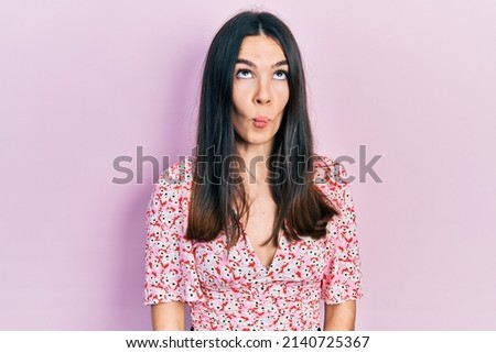 Young brunette woman wearing summer dress making fish face with lips, crazy and comical gesture. funny expression. 