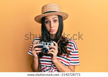 Young hispanic woman wearing summer hat holding vintage camera depressed and worry for distress, crying angry and afraid. sad expression. 