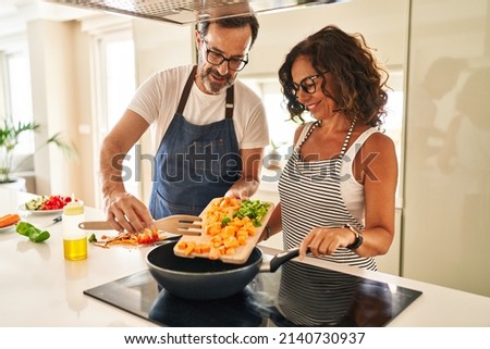 Middle age hispanic couple smiling confident pouring food on frying pan at kitchen Royalty-Free Stock Photo #2140730937