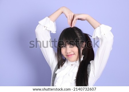 The cute young Asian girl with white preppy dressed style standing on the purple background