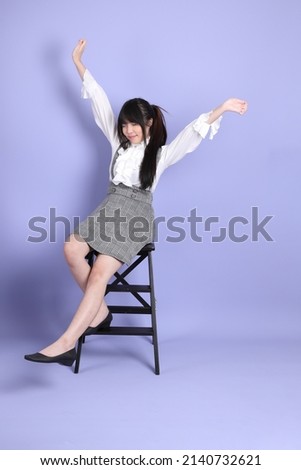 The cute young Asian girl with white preppy dressed style sitting on the purple background