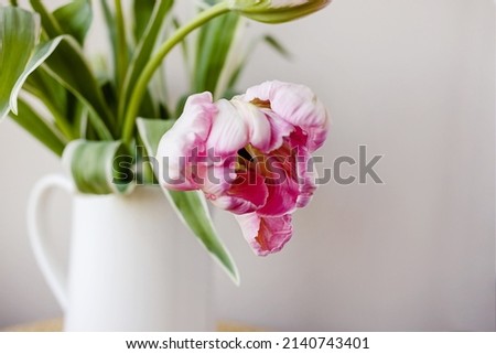 Pink tulip flower bouquet with green fresh stems in a white porcelain jar vase on a white window frame with blue sky background. Vibrant colourful botany floral home decor idea.