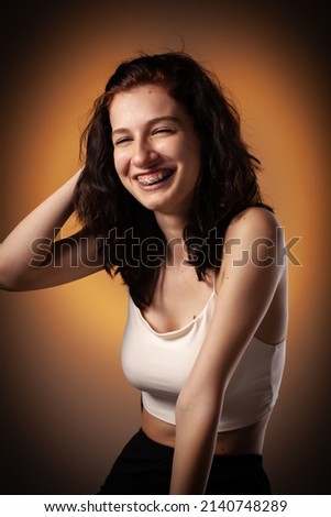 Teenage girl with dental braces. Studio portrait on neon orange colored background.