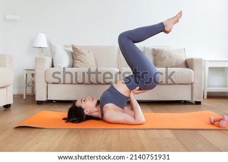 One beautiful Asian woman doing yoga on exercise mat in her living room, lying on upper back and holding her lower back in balance. Royalty-Free Stock Photo #2140751931