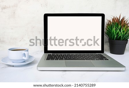 Laptop or notebook with blank screen, coffee and potted plant on white table. Business concept. Copy space.