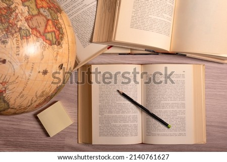 BROWN WOODEN STUDY TABLE. OPEN BOOKS. BLACK PENCIL, STICKY NOTES AND GLOBE.