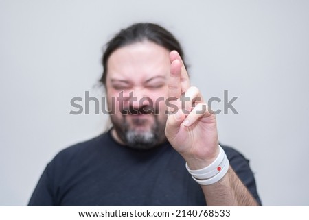 An unshaven man with bracelets in the colors of the Japanese flag makes a gesture with crossed fingers. Selective focus on the bracelet.