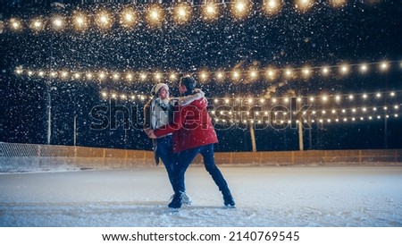 Romantic Winter Snowy Evening: Ice Skating Couple Having Fun on Ice Rink. Pair Skating Boyfrined and Girlfriend in Love, Dance, Spin Embrace, Figure Skate Professionaly at Beautifully Lit Location