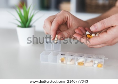 Female elderly hands sorting pills. Closeup of medical pill box with doses of tablets for daily take a medicine with white, yellow drugs and capsules. Young woman getting her daily vitamins at home.  Royalty-Free Stock Photo #2140777343