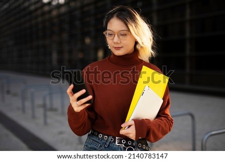 Beautiful Chinese woman with mobile phone walking on the street. Young girl typing a message	