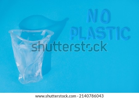hands crumple crumple a plastic cup on a blue background. Ecology concept. no plastic  Royalty-Free Stock Photo #2140786043