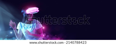 Cyber Space. Excited young Asian lady using VR glasses, looking at empty copy place for mockup, millennial woman experiencing virtual reality isolated on neon studio background, wide panorama banner