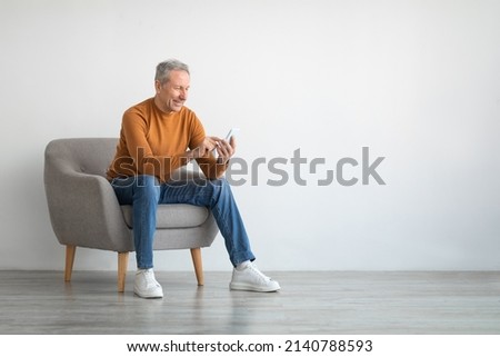 Cheerful Mature Guy Using Mobile Phone Testing New Application Sitting In Armchair Isolated On White Studio Wall Background. Gadgets And Mobile Communication Concept. Free Empty Copy Space For Text Royalty-Free Stock Photo #2140788593