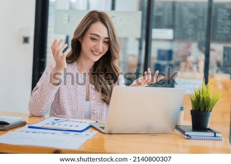 Smiling beautiful Asian businesswoman analyzing charts and graphs showing market changes using laptop at company desk reading financial charts.