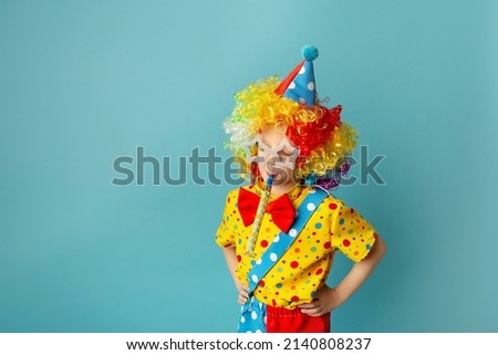 Funny kid clown against blue background. Happy child playing with festive decor. 1 April Fool's day concept.
