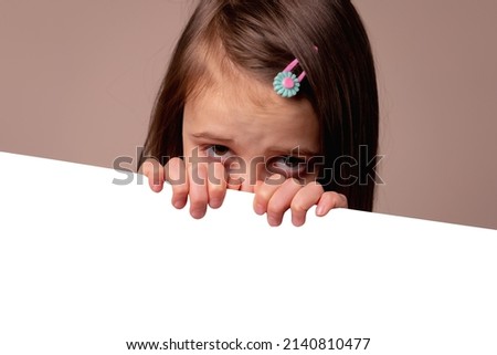 Happy young child girl behind white empty board for design. Copy space. Horizontal image.