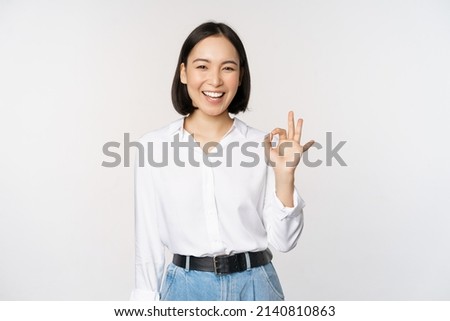 Very good. Smiling asian woman showing okay with satisfied face expression, praise and compliment great job, pleased by smth, standing over white background
