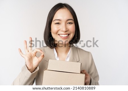 Smiling asian businesswoman, showing okay sign and boxes with delivery goods, prepare order for client, standing over white background