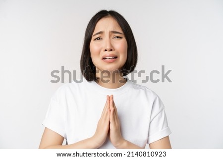 Desperate crying asian woman begging, asking for help, pleading and say please, standing in white t-shirt over white background Royalty-Free Stock Photo #2140810923