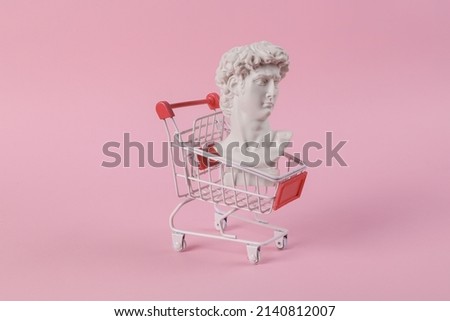 Antique bust of David with shopping trolley on a pink background. Conceptual pop. Minimal shopping still life. Creative idea Royalty-Free Stock Photo #2140812007